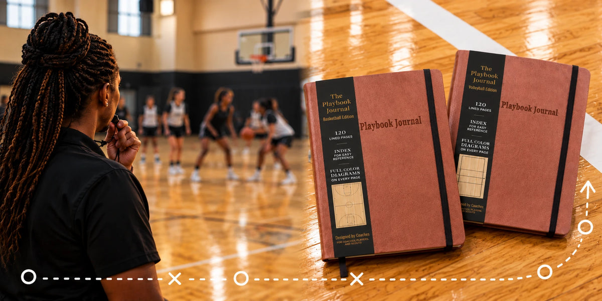 A coach in a black polo blows a whistle and watches a basketball practice in a gym, next to a Basketball Edition and a Volleyball Edition Playbook Journal on a hardwood floor.